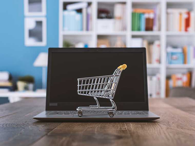 A laptop on a table and a tiny shopping cart on top of the laptop